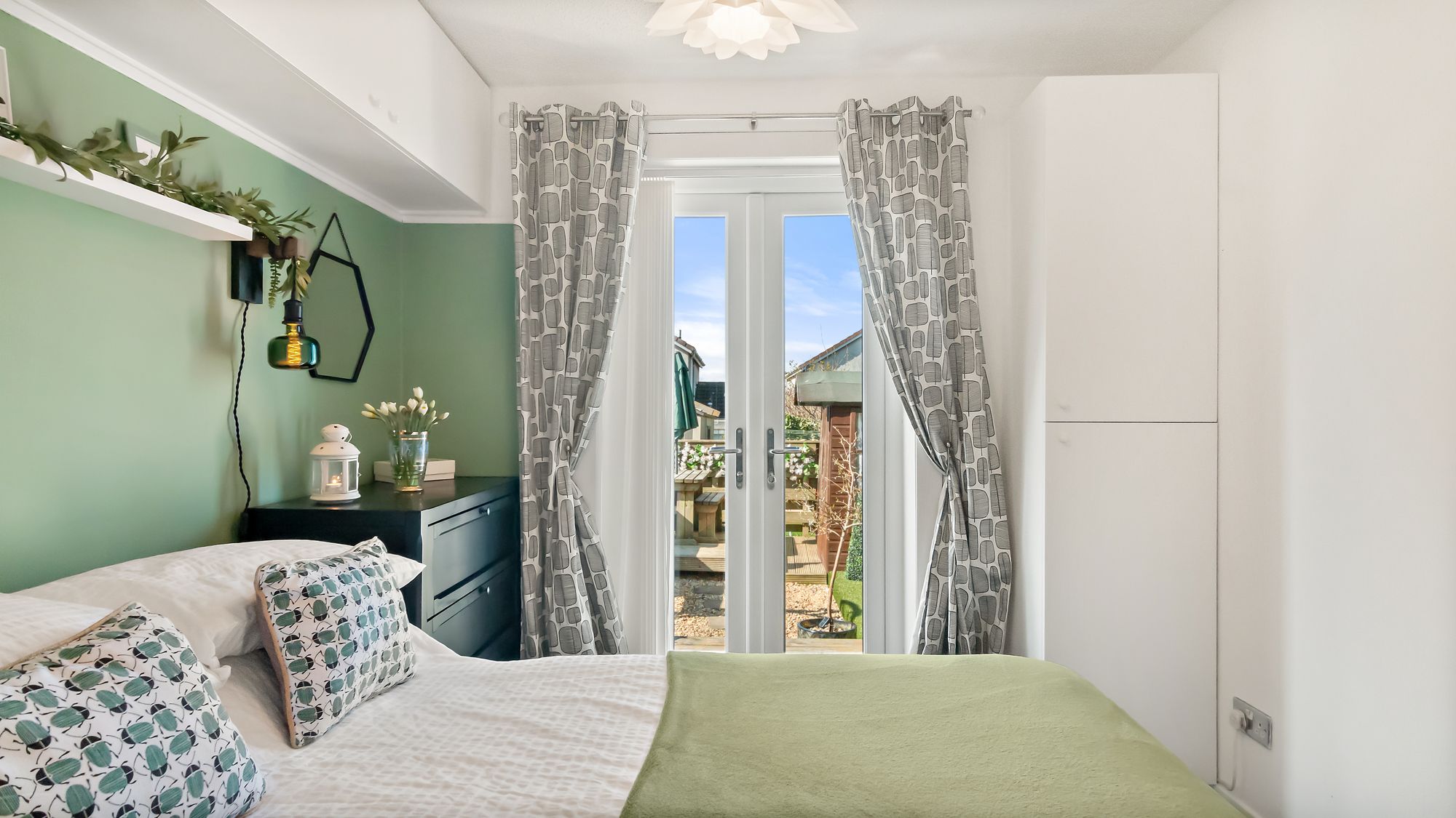 Bedroom in sage green with patio doors onto garden decking