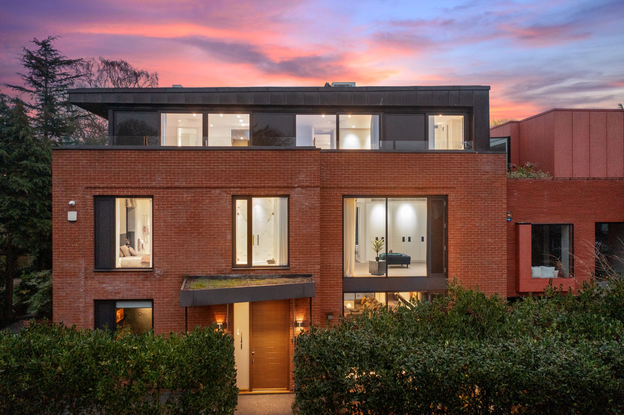 Modern red brick house exterior at dusk with warm interior lighting